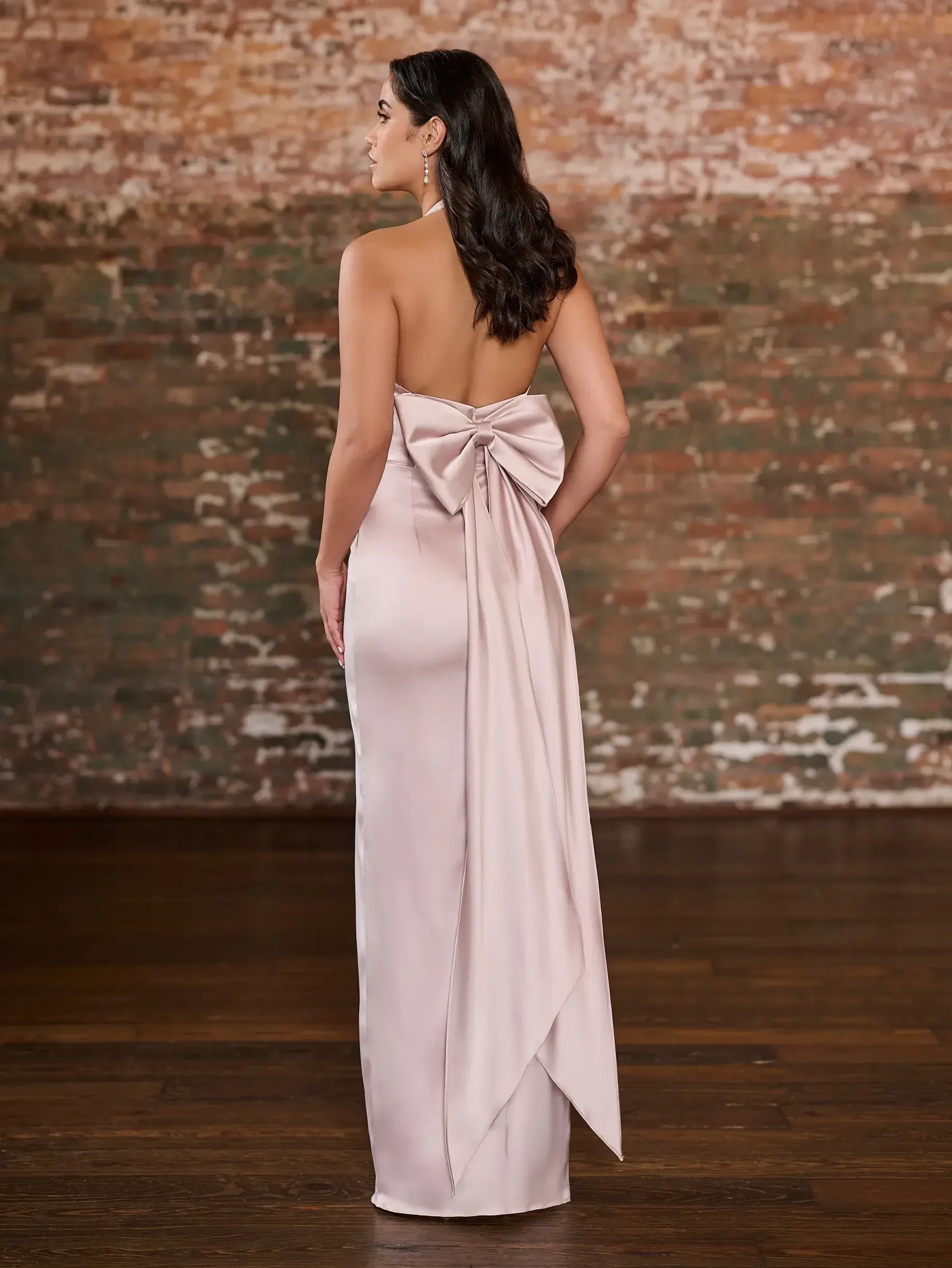 model is wearing a light pink sleeveless bridesmaid dress with a low. back and a bow