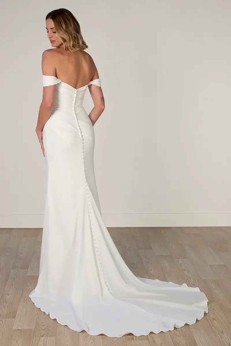 Model is wearing a crepe wedding gown with a column silhouette and scooped neckline