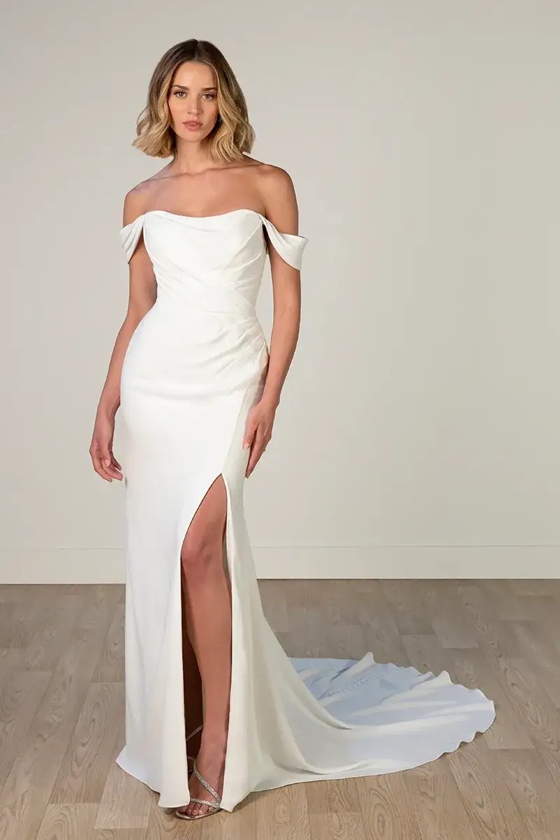 Model is wearing a crepe wedding gown with a column silhouette and scooped neckline