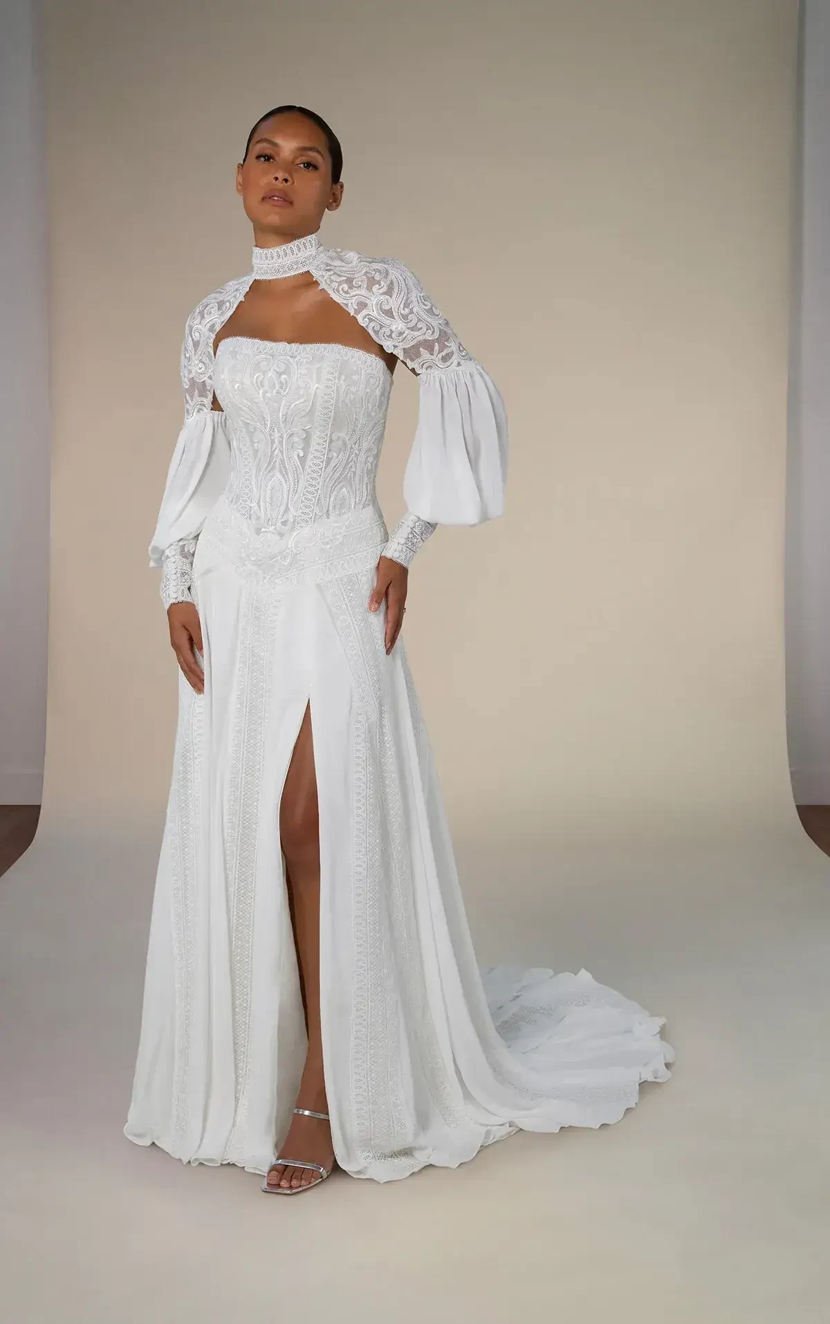 A person wearing a white gown with a high slit and long, puffed sleeves, complemented by a matching lace shawl. The background is neutral, highlighting the outfit.