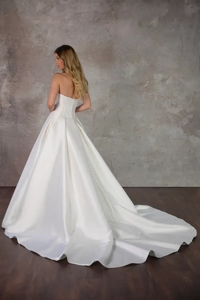 Model is wearing a satin ball gown bridal dress with a strapless neckline and optional belt