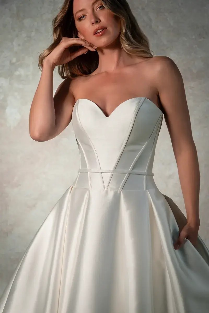 Model is wearing a satin ball gown bridal dress with a strapless neckline and optional belt