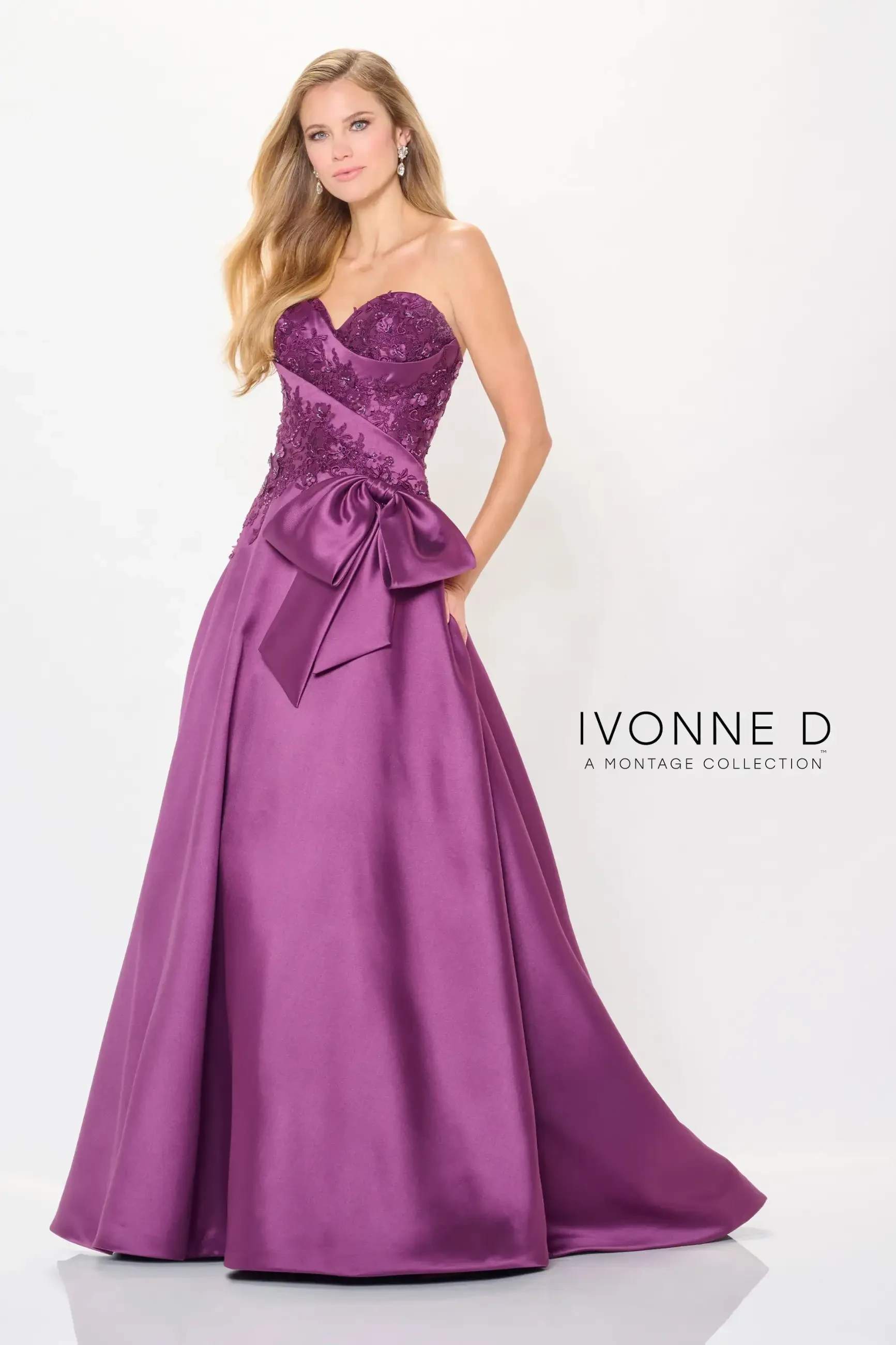 A woman in a strapless purple gown with lace detailing and a large bow poses gracefully. The dress has a fitted bodice and flowing skirt. Text reads 