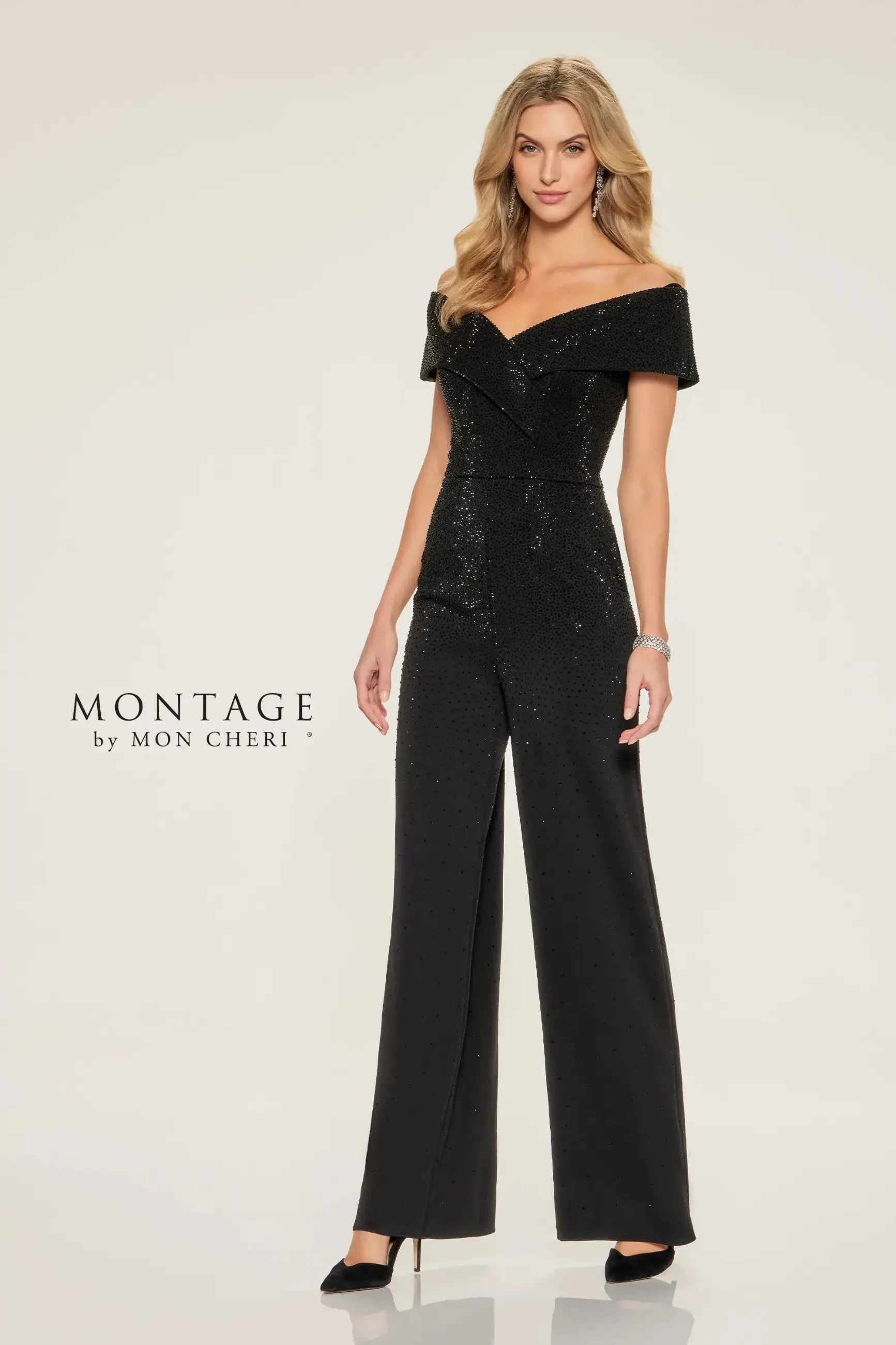 Woman in an elegant off-shoulder black jumpsuit with shimmering details stands confidently. Her expression is poised. 