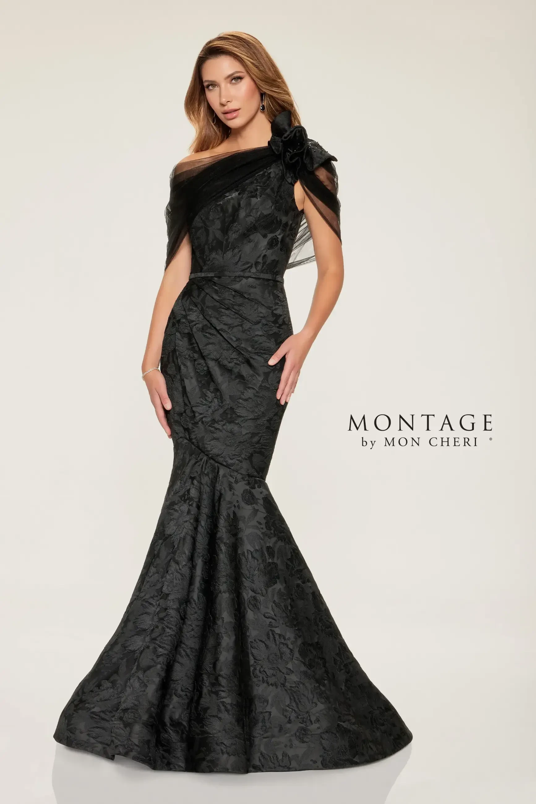 A woman poses in an elegant, off-shoulder black floral gown with a fitted bodice and flared skirt. She exudes confidence and sophistication. 
